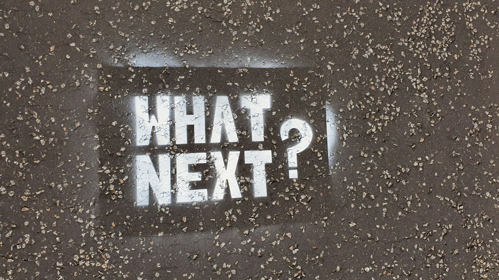 暗い舗装の上に白いステンシルで書かれた「what next」の文字